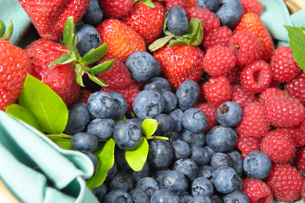 Pile of blueberries, raspberries, and strawberries in a basket.