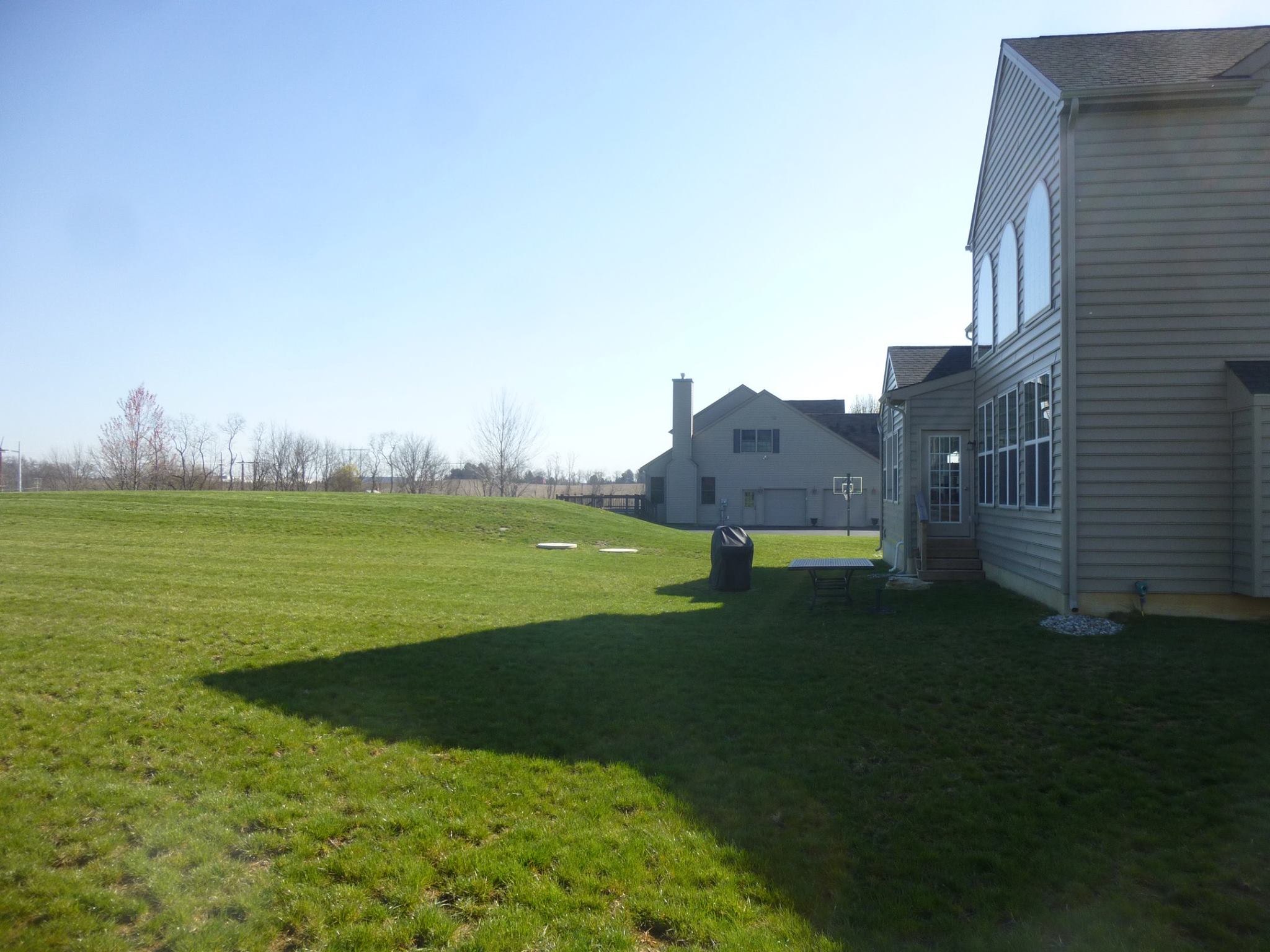 Side view of backyard with homes in background, lots of grass.