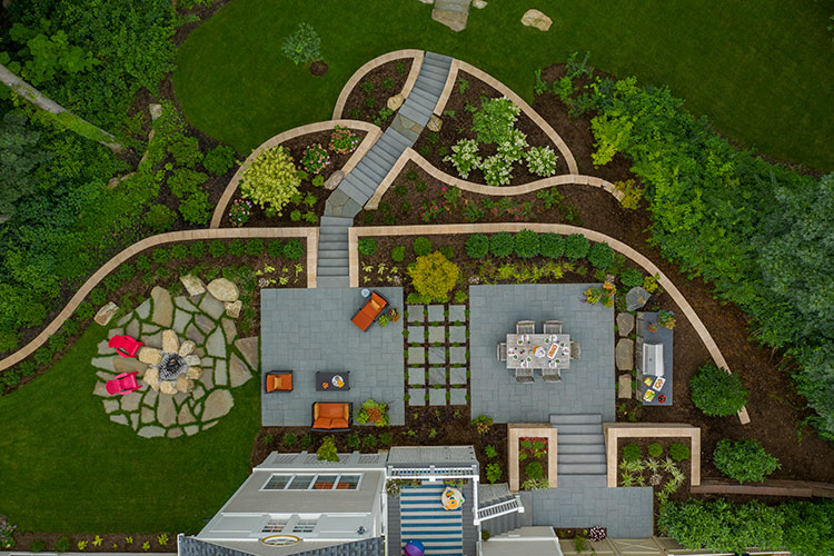 Aerial View of a backyard landscape with red chairs, lush grass and stone hardscape walkways.